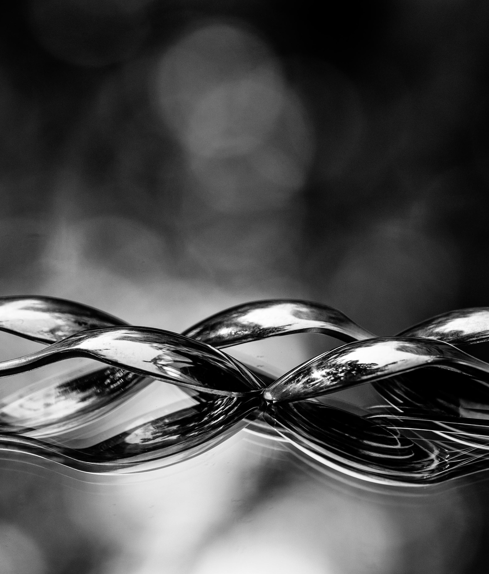 black and white image of spoons reflected on a mirror appearing intertwined against a beautiful bokeh background