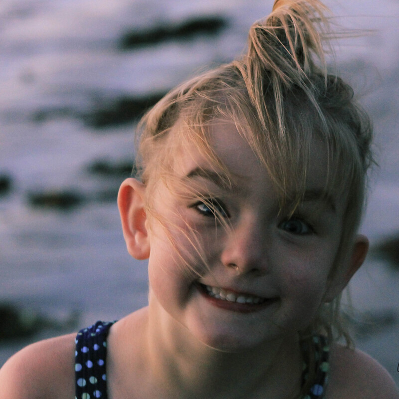 portrait of a young smiling blond girl at a windy beach 