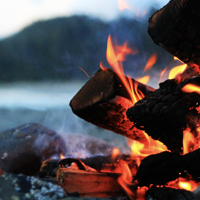 Closeup of a beach fire with a blurred background of sand, water and a rocky outcrop